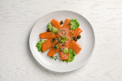 Photo of Salmon carpaccio with capers, lettuce, microgreens and onion on white wooden table, top view