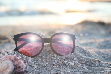 Photo of Stylish sunglasses on sandy beach at sunset