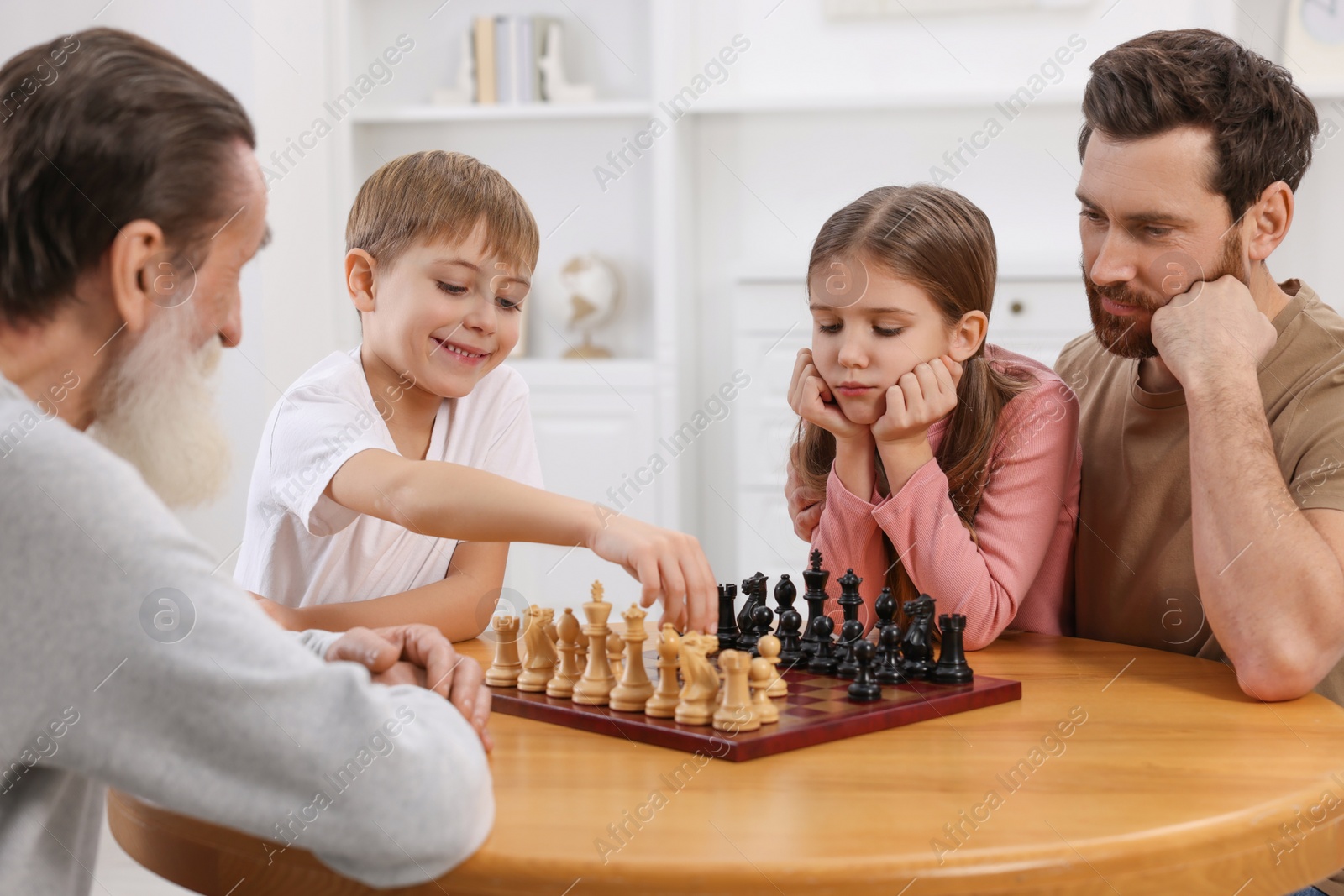 Photo of Family playing chess together at table in room