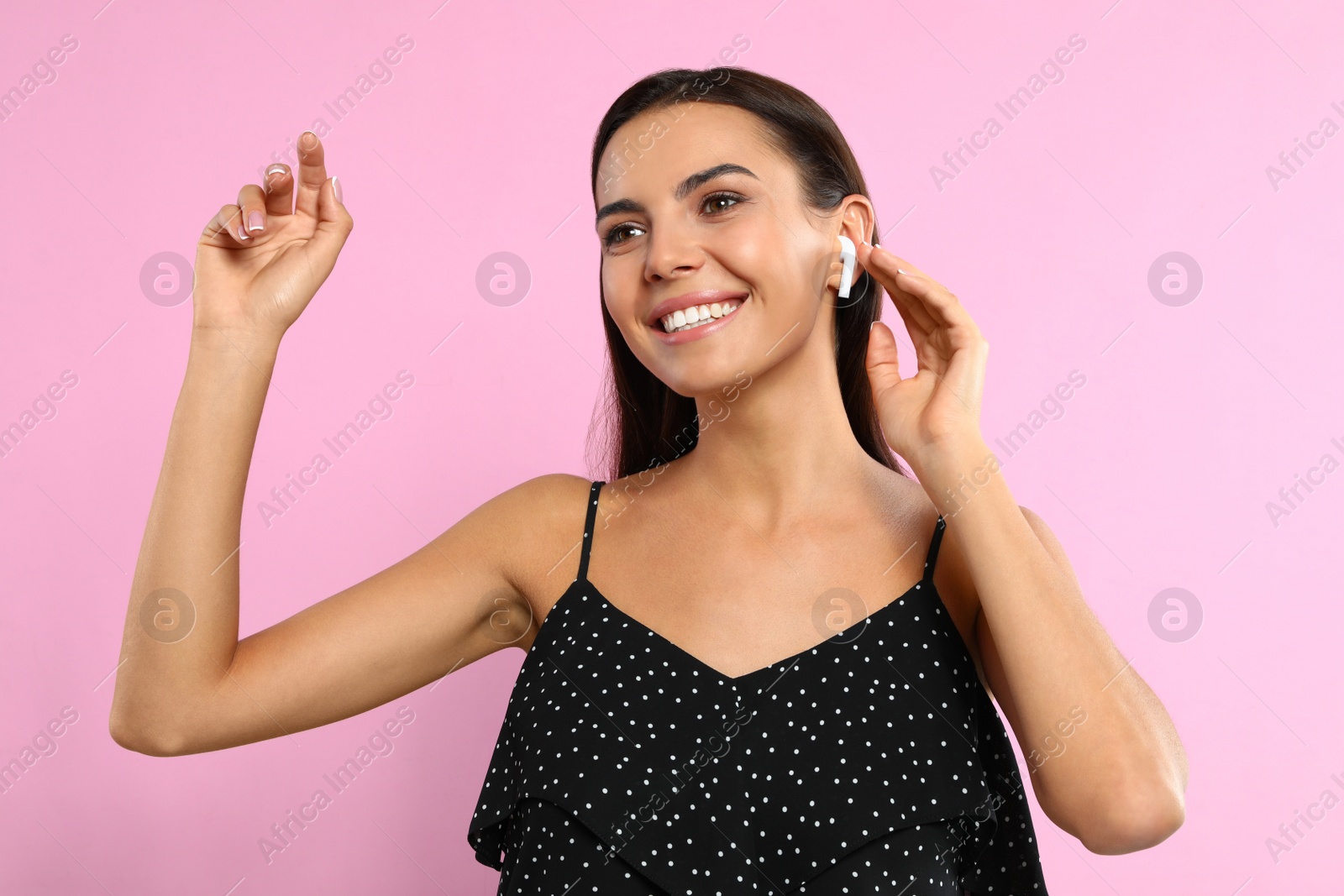 Photo of Happy young woman listening to music through wireless earphones on pink background