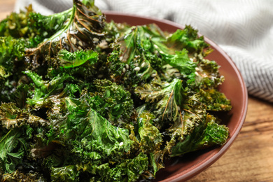 Photo of Tasty baked kale chips on wooden table, closeup