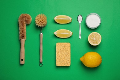 Cleaning supplies for washing dishes on green background, flat lay