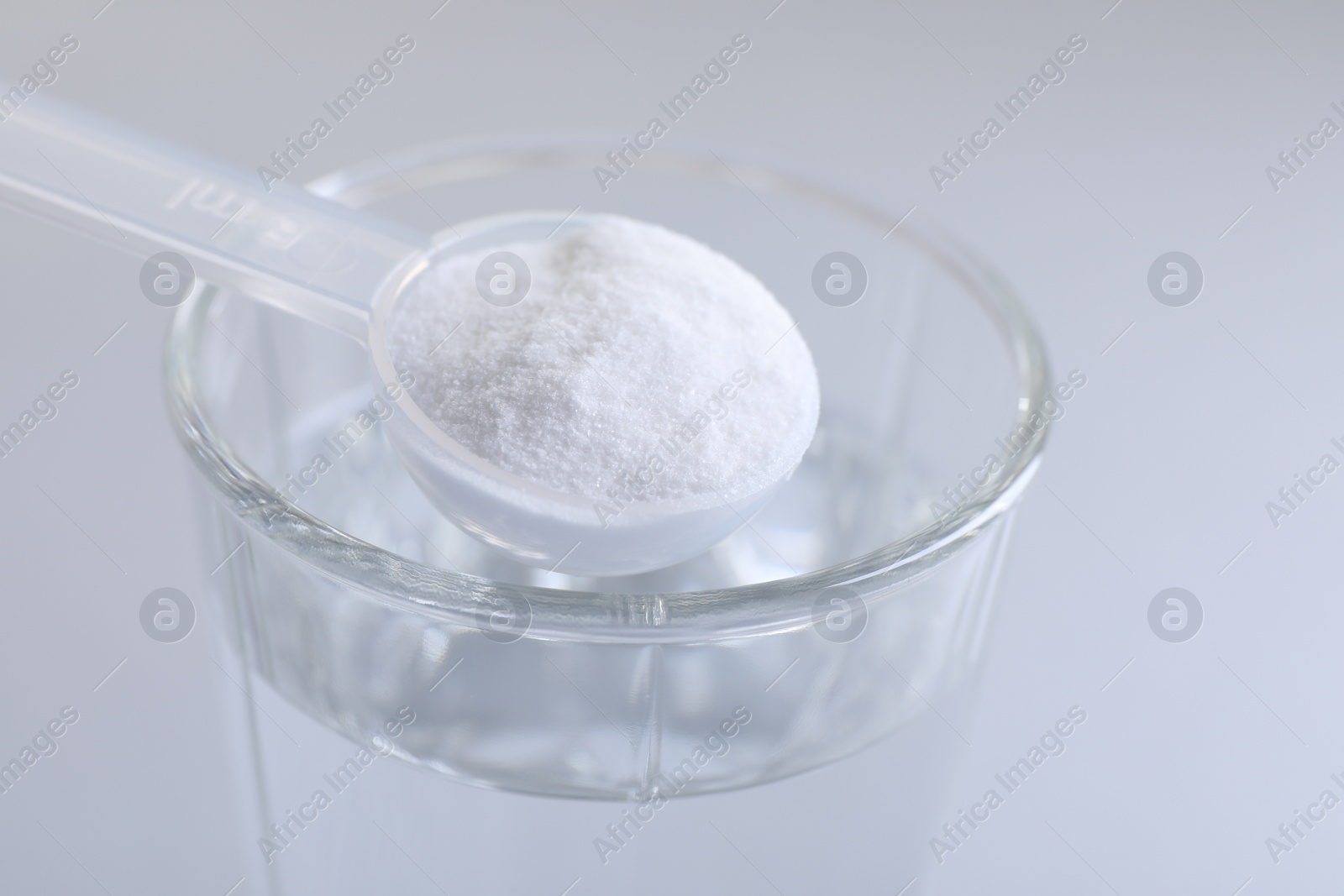 Photo of Spoon with baking soda over glass of water on light grey background, closeup