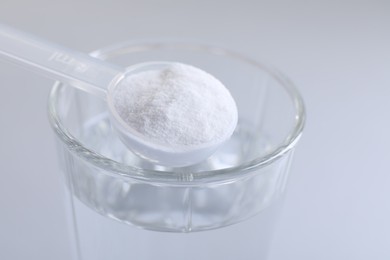 Photo of Spoon with baking soda over glass of water on light grey background, closeup