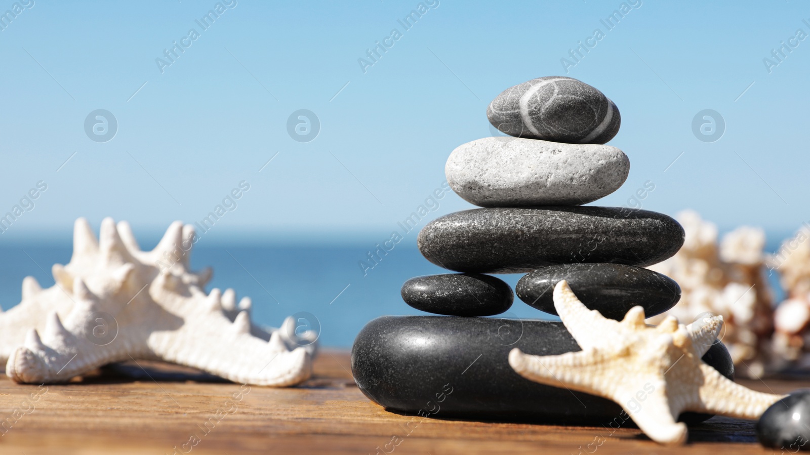 Photo of Stack of stones and starfishes on wooden pier near sea, space for text Zen concept