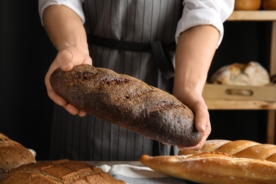 Baker holding loaf of bread over table indoors, closeup