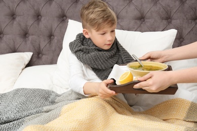 Photo of Young woman bringing broth to her sick son in bed. Cold treatment