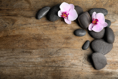 Photo of Stones with orchid flowers and space for text on wooden background, flat lay. Zen lifestyle