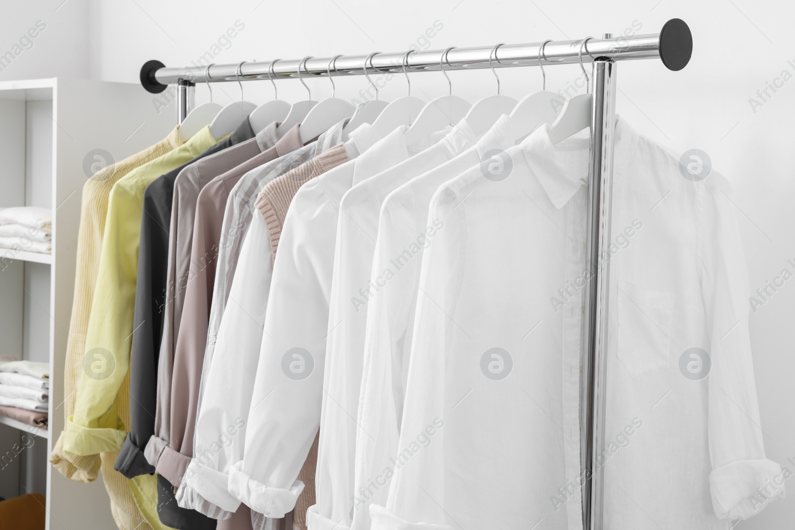 Photo of Wardrobe organization. Rack with different stylish clothes near white wall indoors