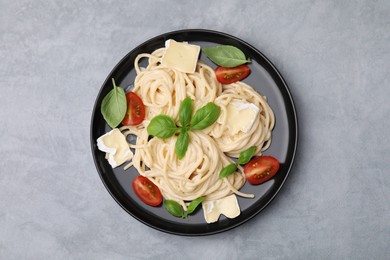 Photo of Delicious pasta with brie cheese, tomatoes and basil leaves on grey table, top view