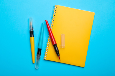 Photo of Yellow notebook and markers on light blue background, flat lay