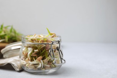 Photo of Mung bean sprouts in glass jar on white table, closeup. Space for text