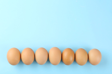 Photo of Raw chicken eggs on light blue background, flat lay. Space for text