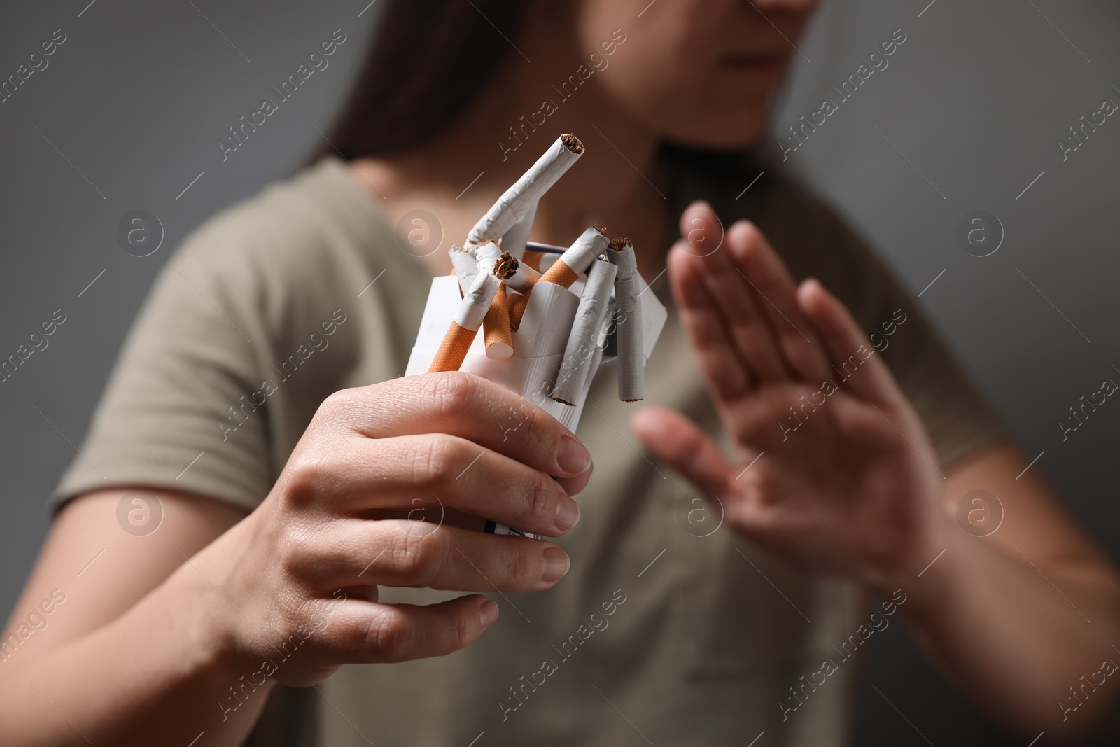 Photo of Stop smoking. Woman holding pack with broken cigarettes on grey background, closeup