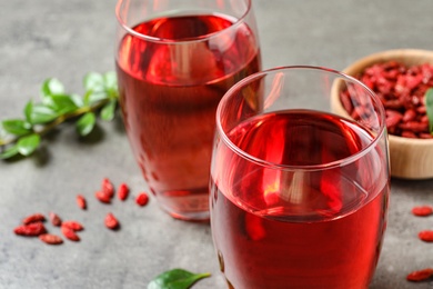 Photo of Glasses of healthy goji juice on grey table, closeup. Space for text