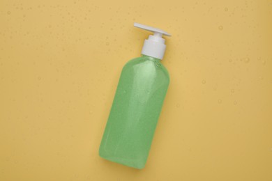 Photo of Wet bottle of face cleansing product on pale orange background, top view