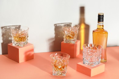 Stylish presentation of whiskey with ice cubes in glasses and bottle on color background