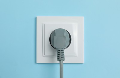 Photo of Power socket with inserted plug on light blue wall, closeup. Electrical supply