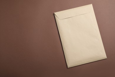 Photo of Kraft paper envelope on brown background, top view. Space for text