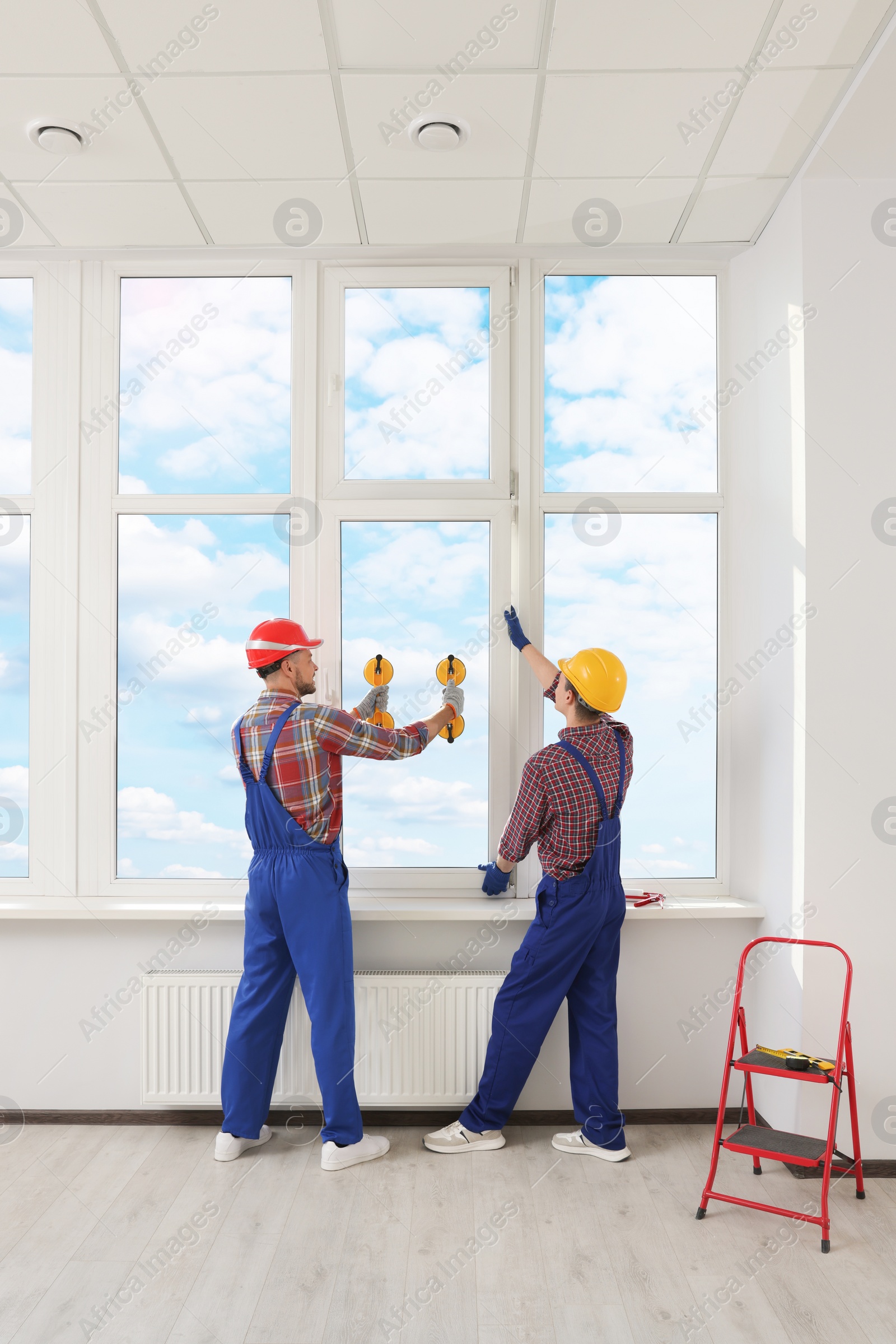 Photo of Workers using suction lifters during plastic window installation indoors