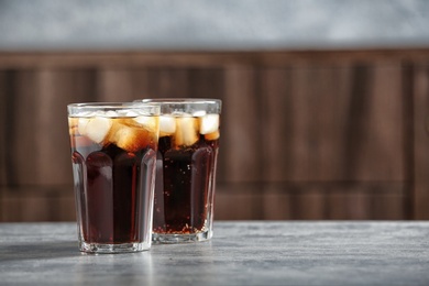 Glasses of cold cola on table against blurred background. Space for text