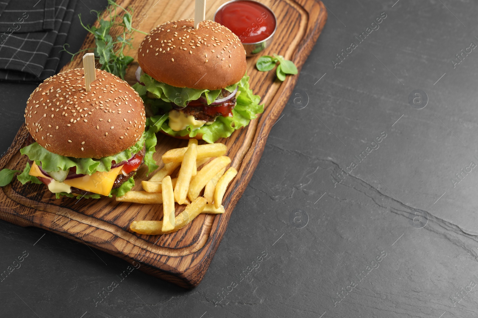 Photo of Delicious burgers with beef patty, tomato sauce and french fries on dark table, above view. Space for text