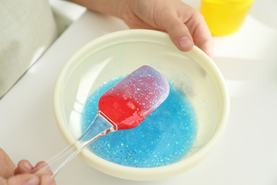 Little girl mixing ingredients with silicone spatula at table, closeup. DIY slime toy