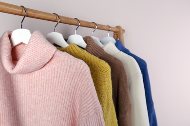 Photo of Warm sweaters hanging on wooden rack against light background, closeup