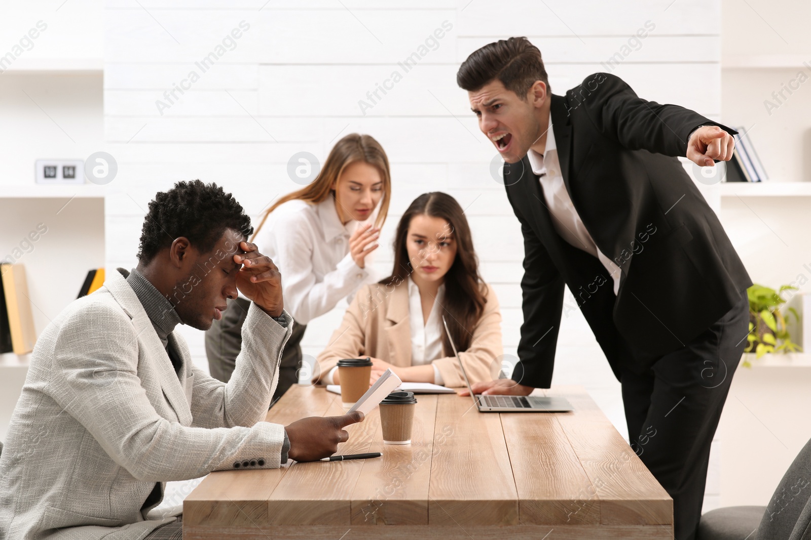 Photo of Man screaming at African American coworker in office. Racism concept