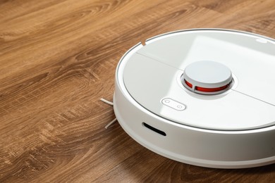Photo of Robotic vacuum cleaner on wooden floor indoors, closeup. Space for text