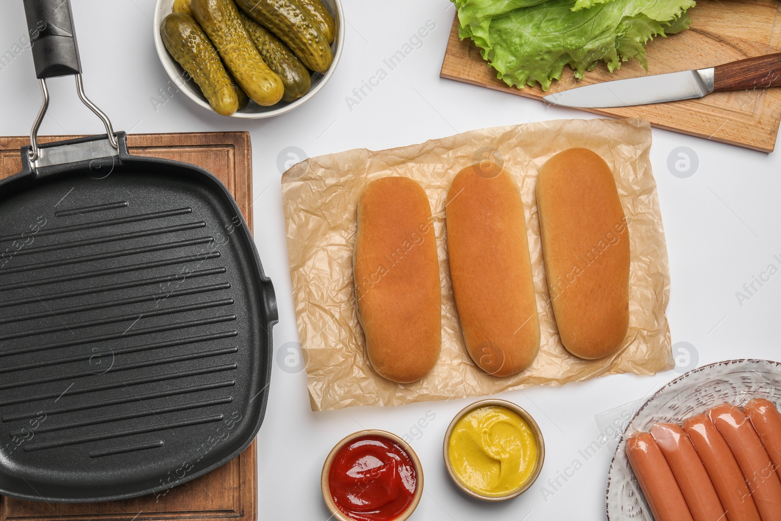 Photo of Different tasty ingredients for hot dog and grill pan on white table, flat lay