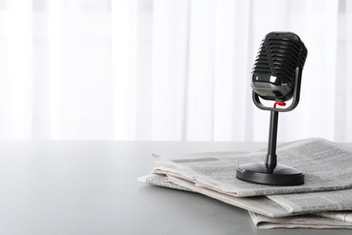 Photo of Newspapers and vintage microphone on grey table, space for text. Journalist's work