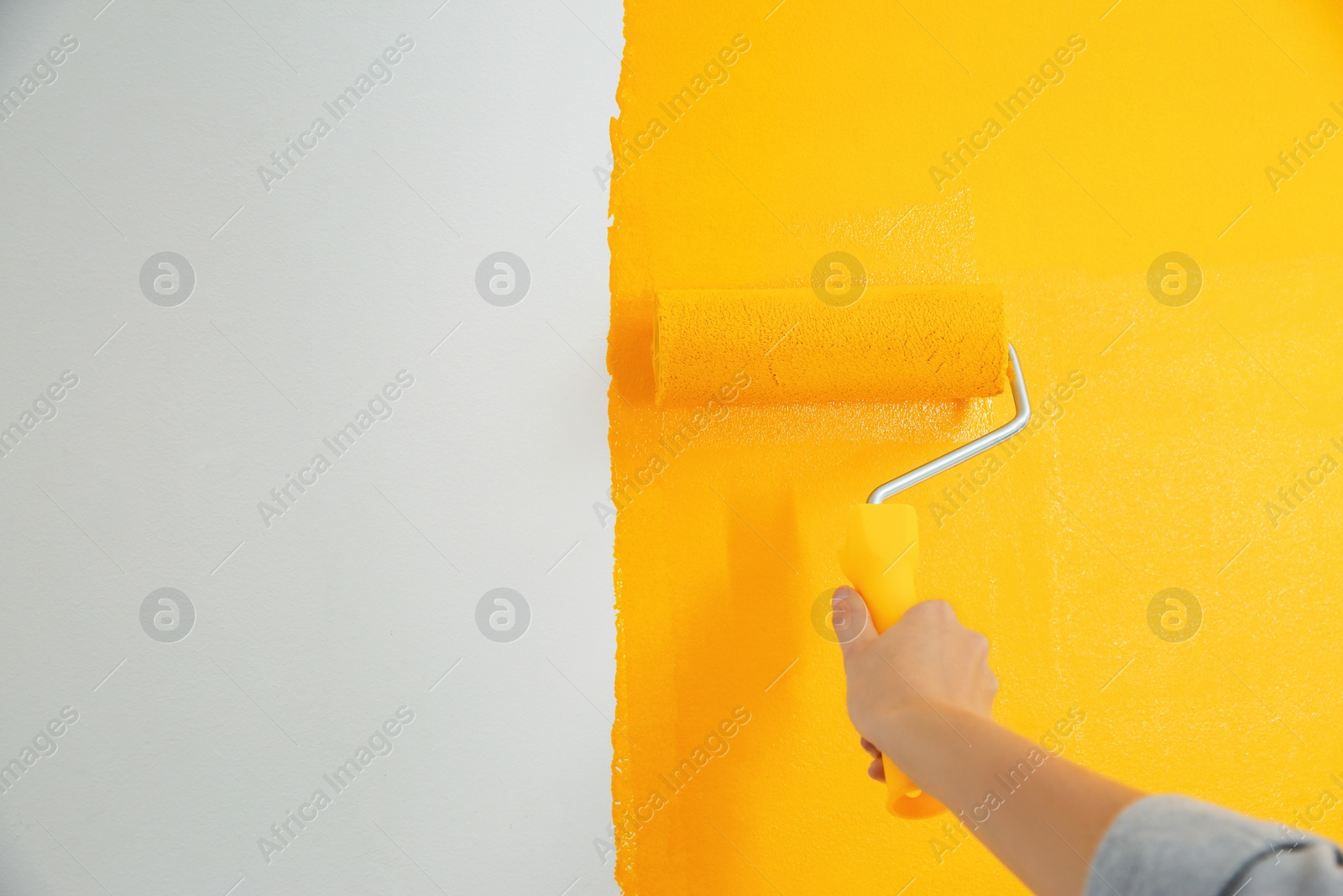 Photo of Woman painting white wall with yellow dye, closeup. Interior renovation