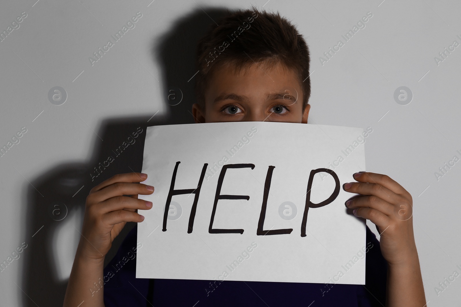 Photo of Abused little boy with sign HELP near white wall. Domestic violence concept