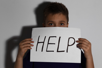 Abused little boy with sign HELP near white wall. Domestic violence concept