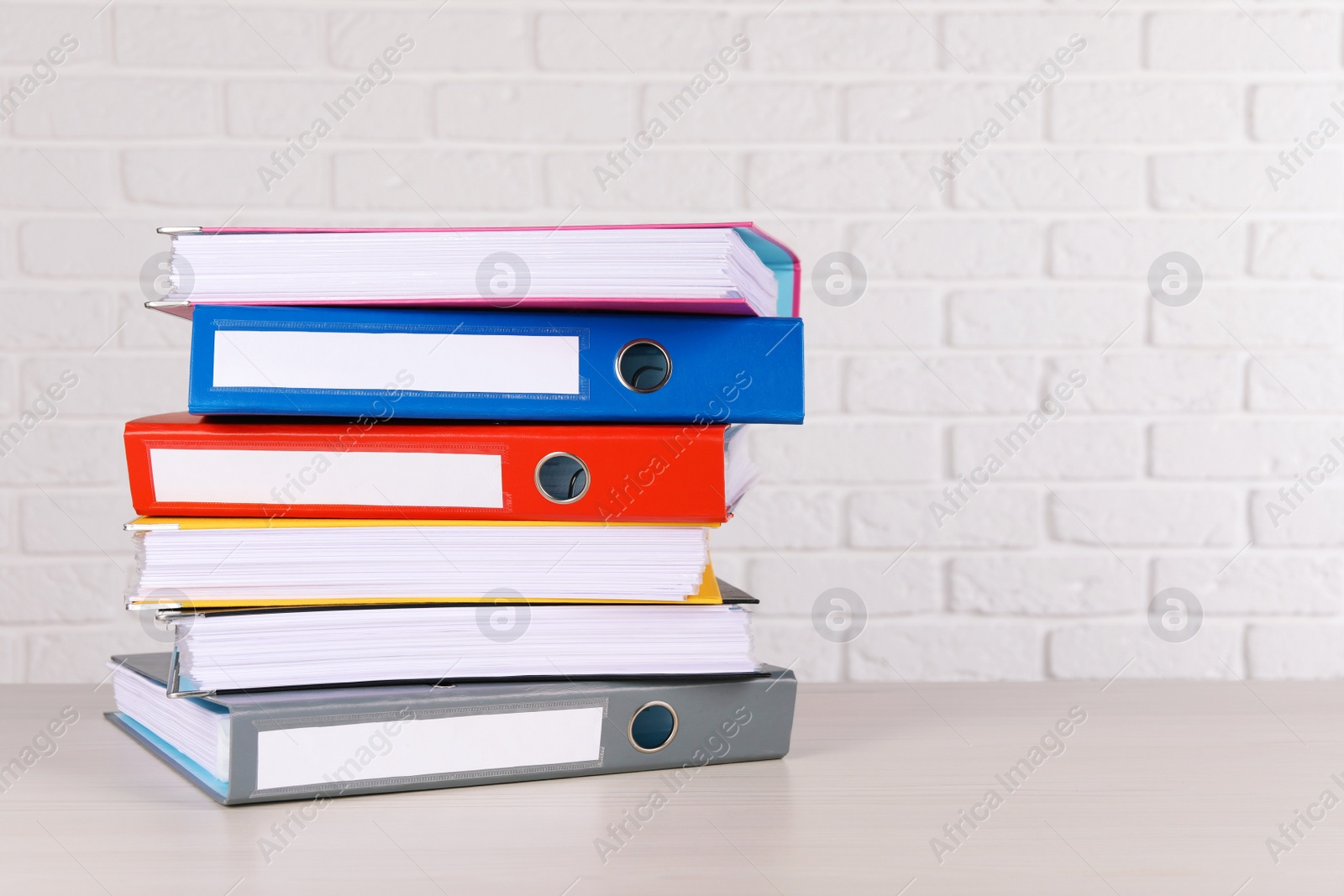 Photo of Stack of office folders on wooden table near white brick wall, space for text