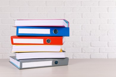 Stack of office folders on wooden table near white brick wall, space for text