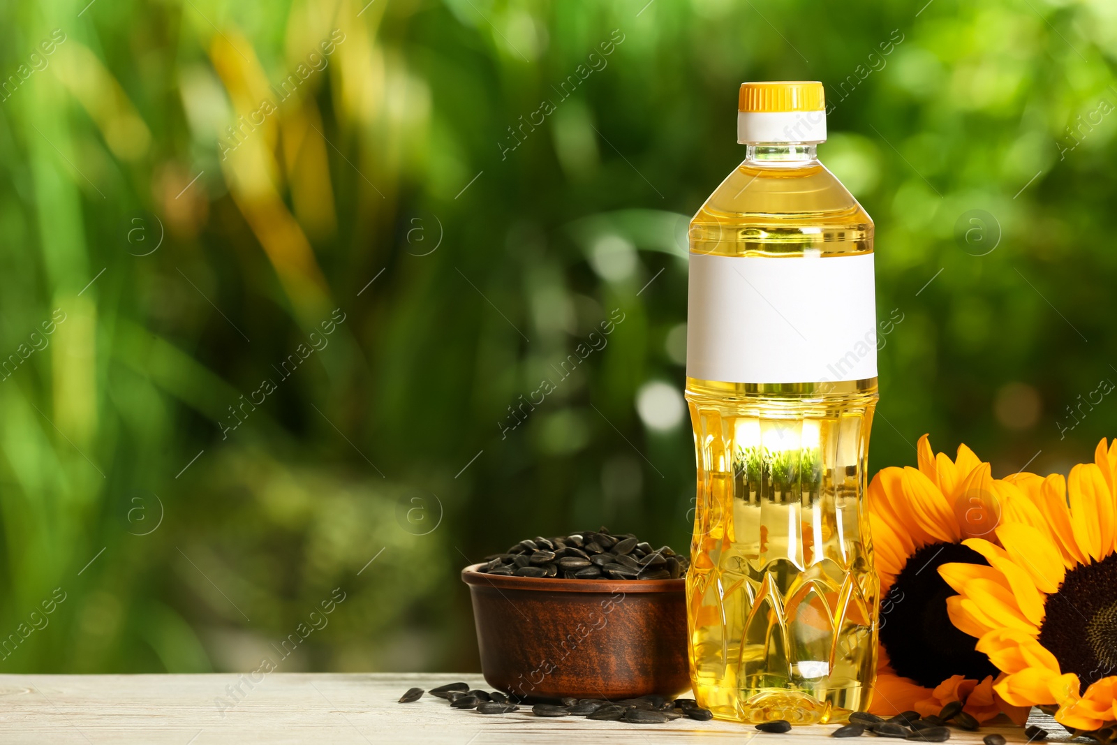 Photo of Sunflower cooking oil, seeds and yellow flowers on white wooden table outdoors, space for text