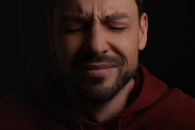 Photo of Sad man crying on black background, closeup