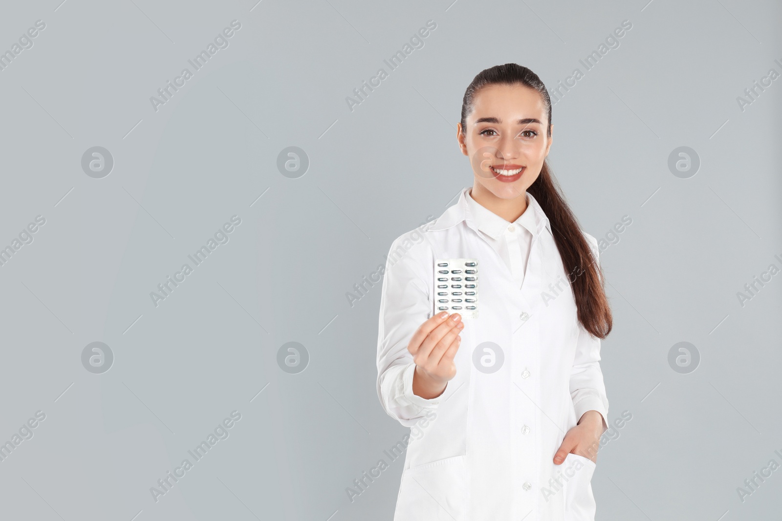 Photo of Professional pharmacist with pills on light grey background. Space for text