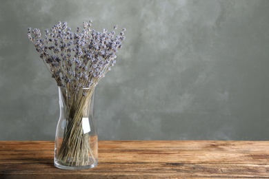 Dried lavender flowers in glass vase on wooden table against grey background. Space for text