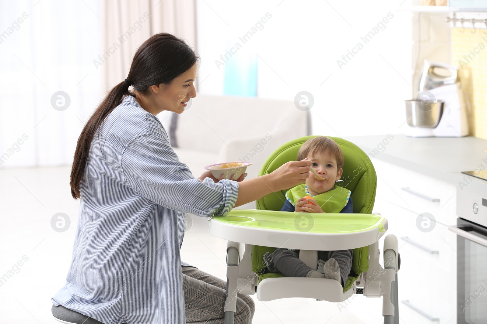 Photo of Young nanny feeding cute little baby in kitchen