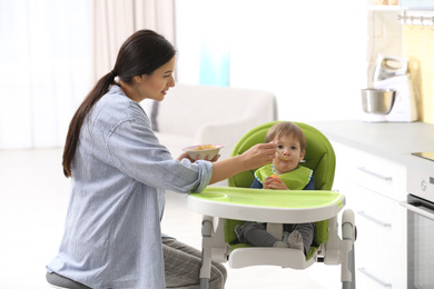 Photo of Young nanny feeding cute little baby in kitchen