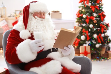 Photo of Authentic Santa Claus with glass of milk reading book indoors