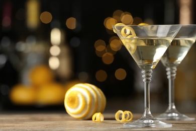 Photo of Glasses of Lemon Drop Martini cocktail with zest on wooden table against blurred background. Space for text