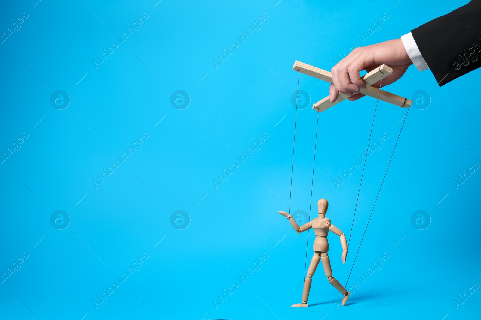 Photo of Man pulling strings of puppet on light blue background, closeup. Space for text