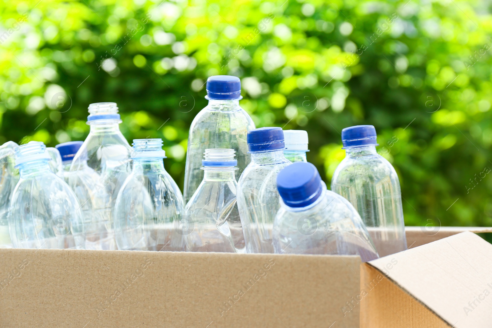 Photo of Cardboard box with used plastic bottles outdoors. Recycle concept