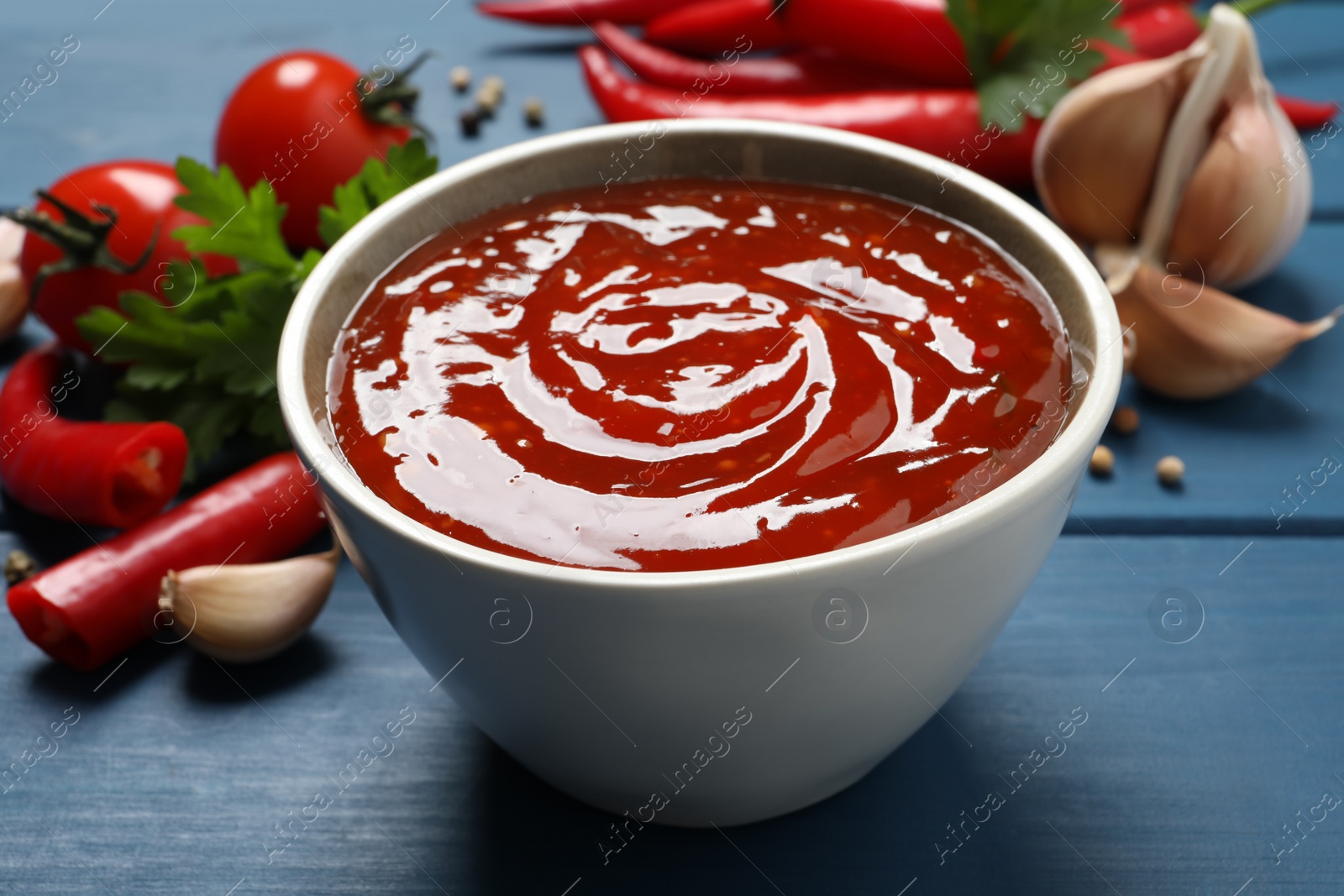 Photo of Spicy chili sauce in bowl on blue wooden table, closeup