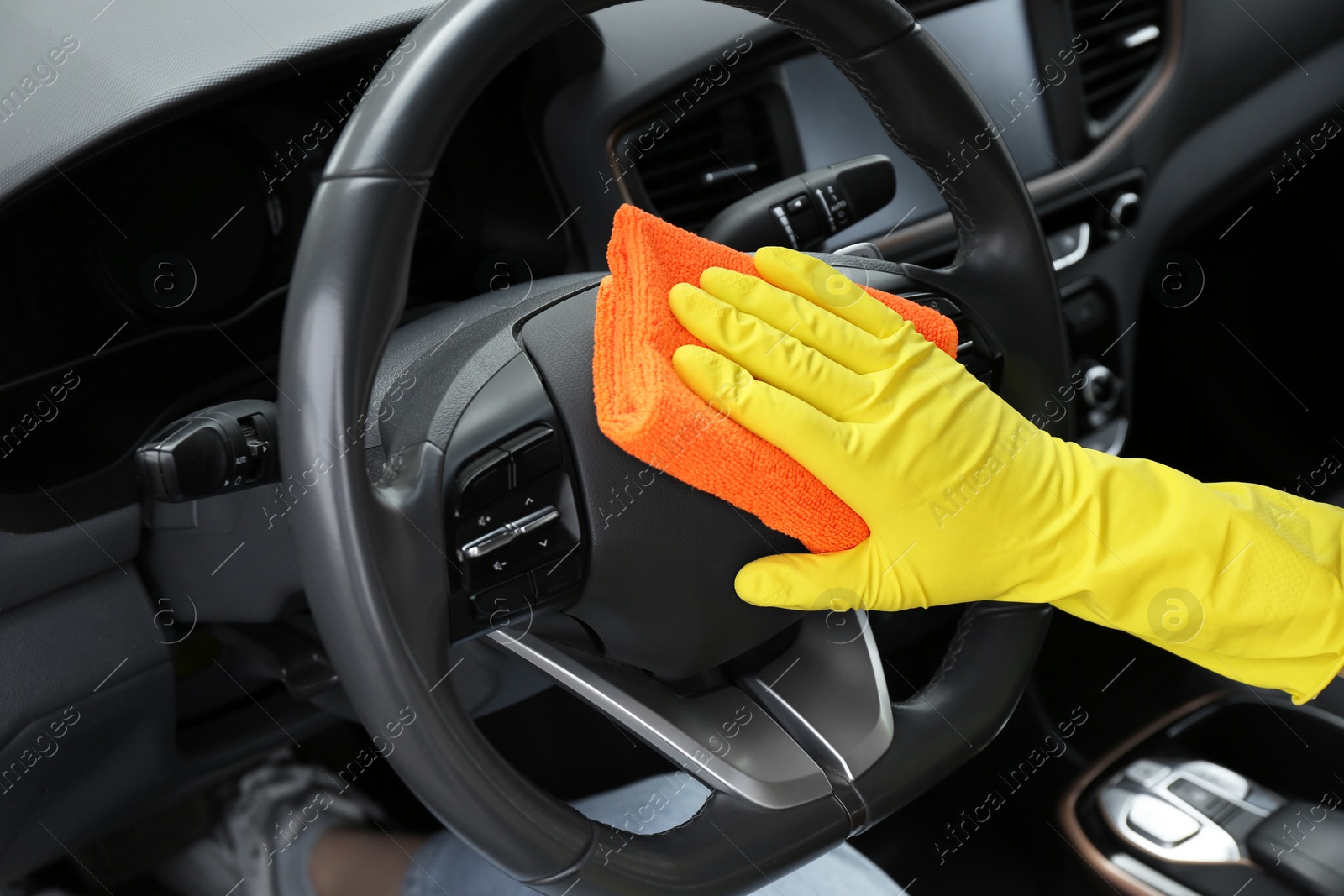 Photo of Woman cleaning steering wheel with rag in car, closeup