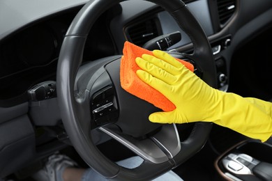 Photo of Woman cleaning steering wheel with rag in car, closeup